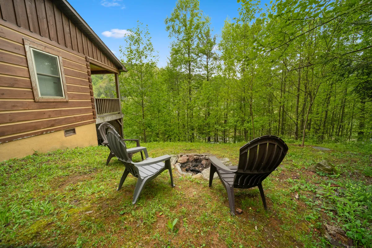 A cozy outdoor fire pit is surrounded by Adirondack chairs, set amidst towering trees. The setup encourages gathering for campfire conversations, stargazing, or roasting marshmallows in the heart of nature.