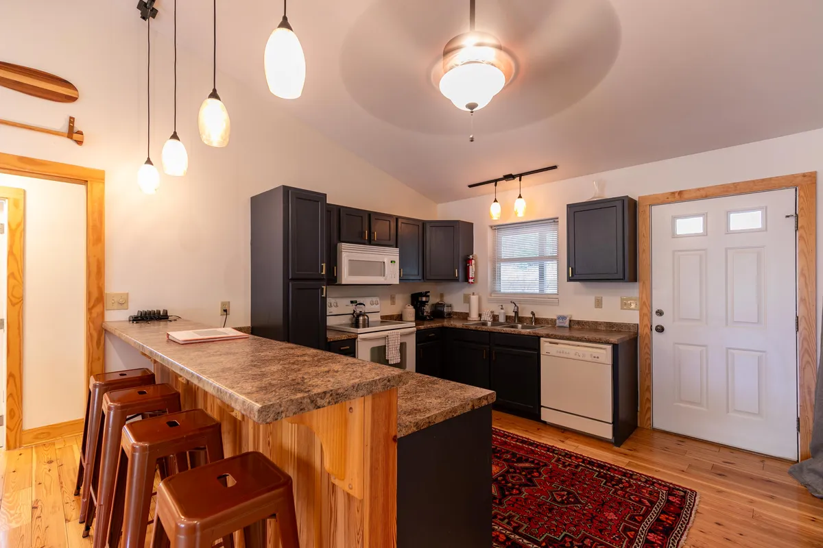 A modern kitchen featuring a central island with bar stools, sleek appliances, and a soft rug. The space is well-lit and open, inviting guests to gather for cooking, casual dining, or conversation.