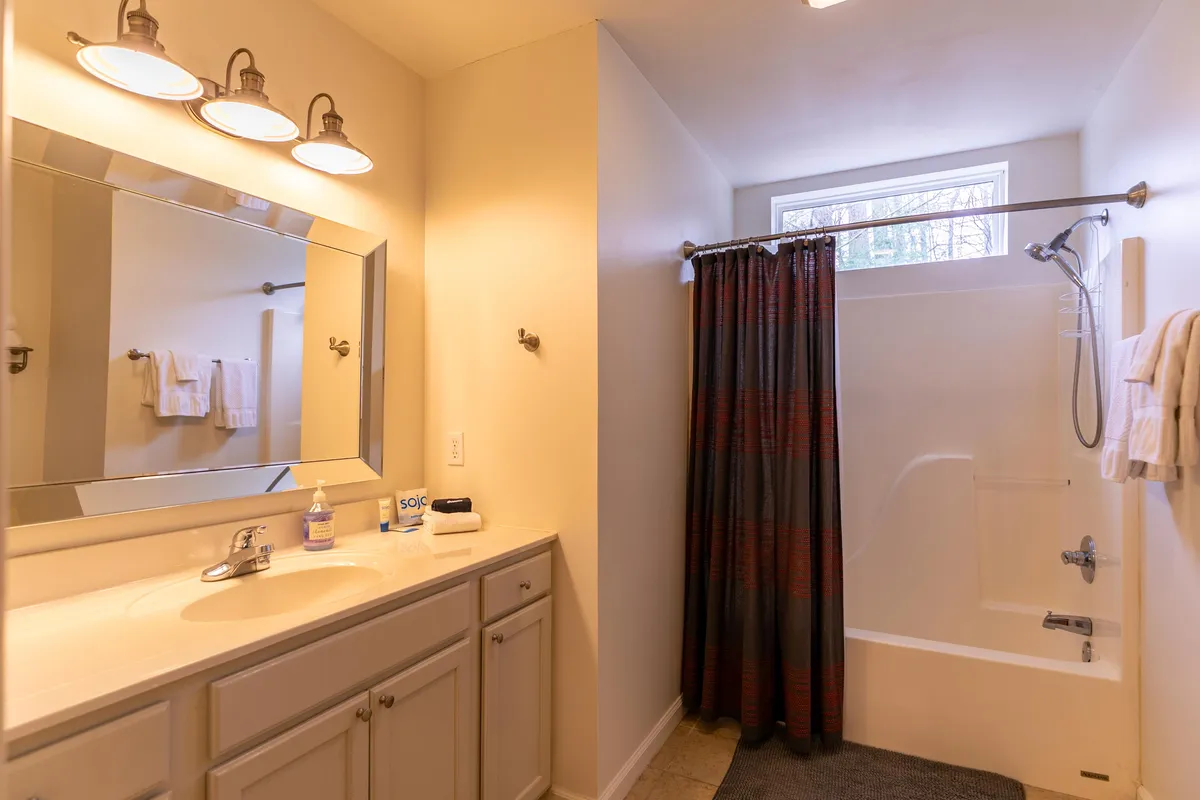 A bright full bathroom featuring a vanity with a large mirror, a spacious shower area, and fresh towels neatly hung on the wall. The modern, clean design creates a refreshing and soothing atmosphere.