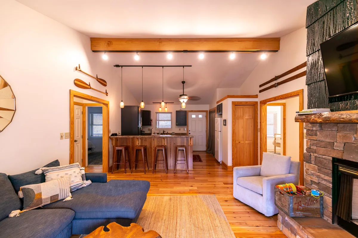 An inviting living and kitchen area with a cozy sofa, a kitchen island, and a fireplace. Ample light fills the space, highlighting the comfortable, open layout ideal for group gatherings and relaxed mornings.