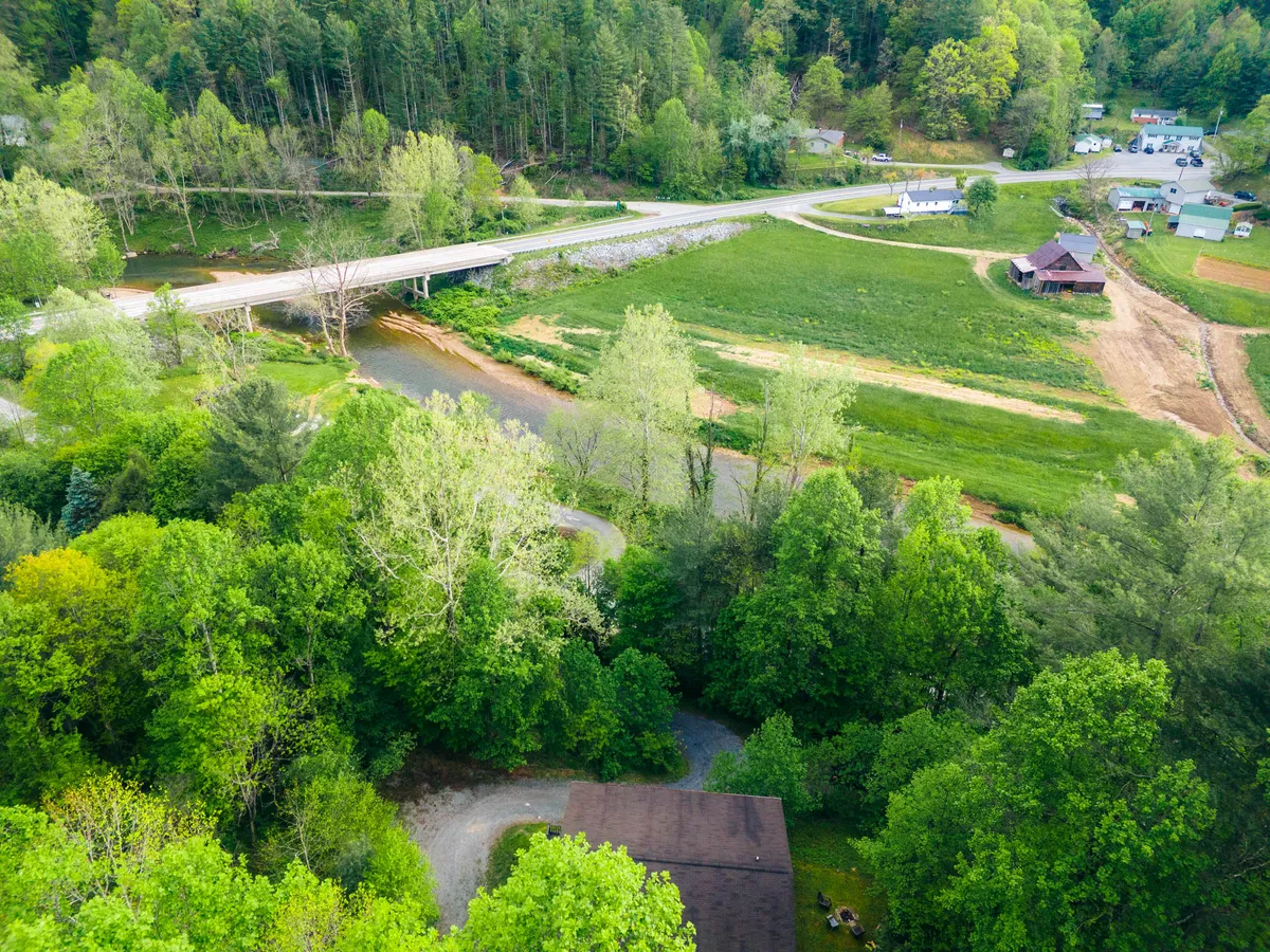 A peaceful river scene with a gently flowing river, lush green trees, a picturesque bridge, and open farmland in the background. The setting feels serene and inviting, ideal for riverside walks, fetch, and relaxation along the water.