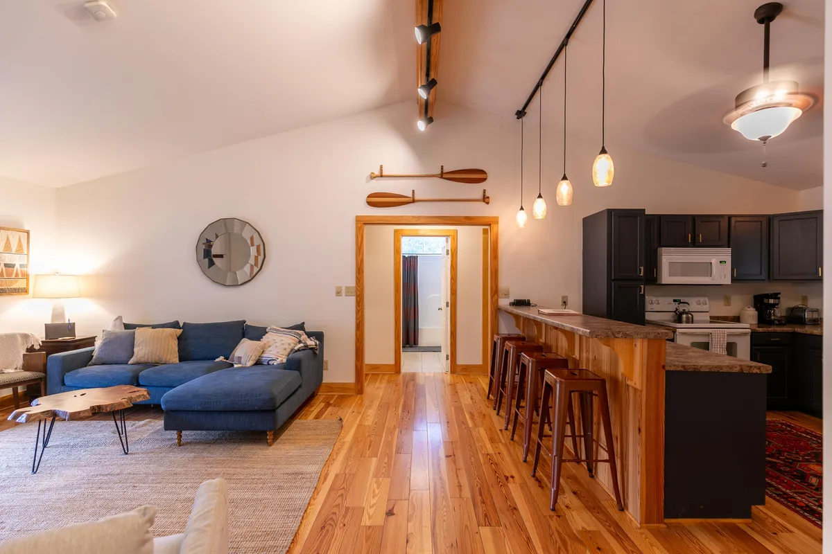 A stylish living area with a blue sectional sofa, a wooden coffee table, pendant lighting, and a view of the kitchen bar area. Nautical accents and thoughtful decor make the space feel both cozy and refined.